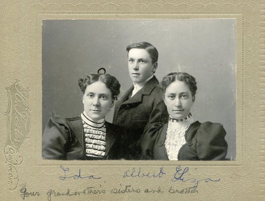 Photograph of two young women and one young man. Handwritten caption at bottom.