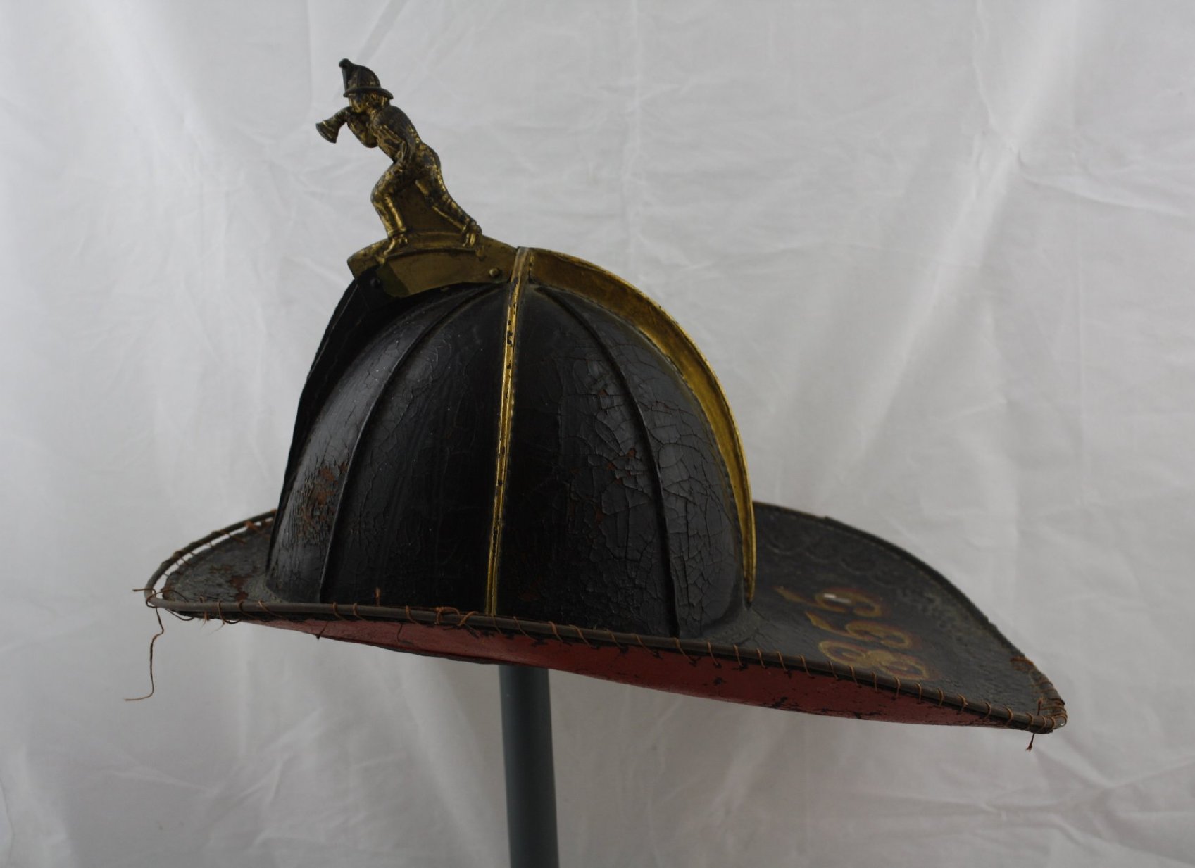  black fireman's helmet hat with red underneath and a gold figure of a man blowing a fire horn.