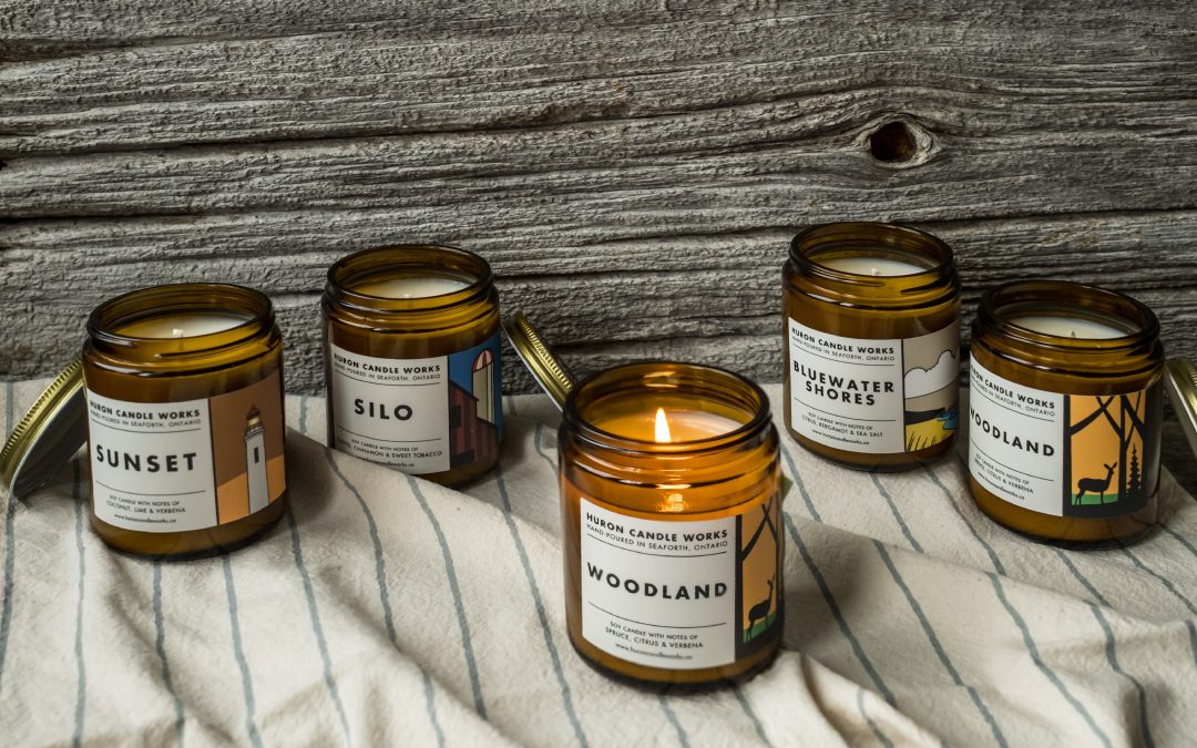 Photo of five candles in amber glass jars featuring the different scents available from Huron Candle Works