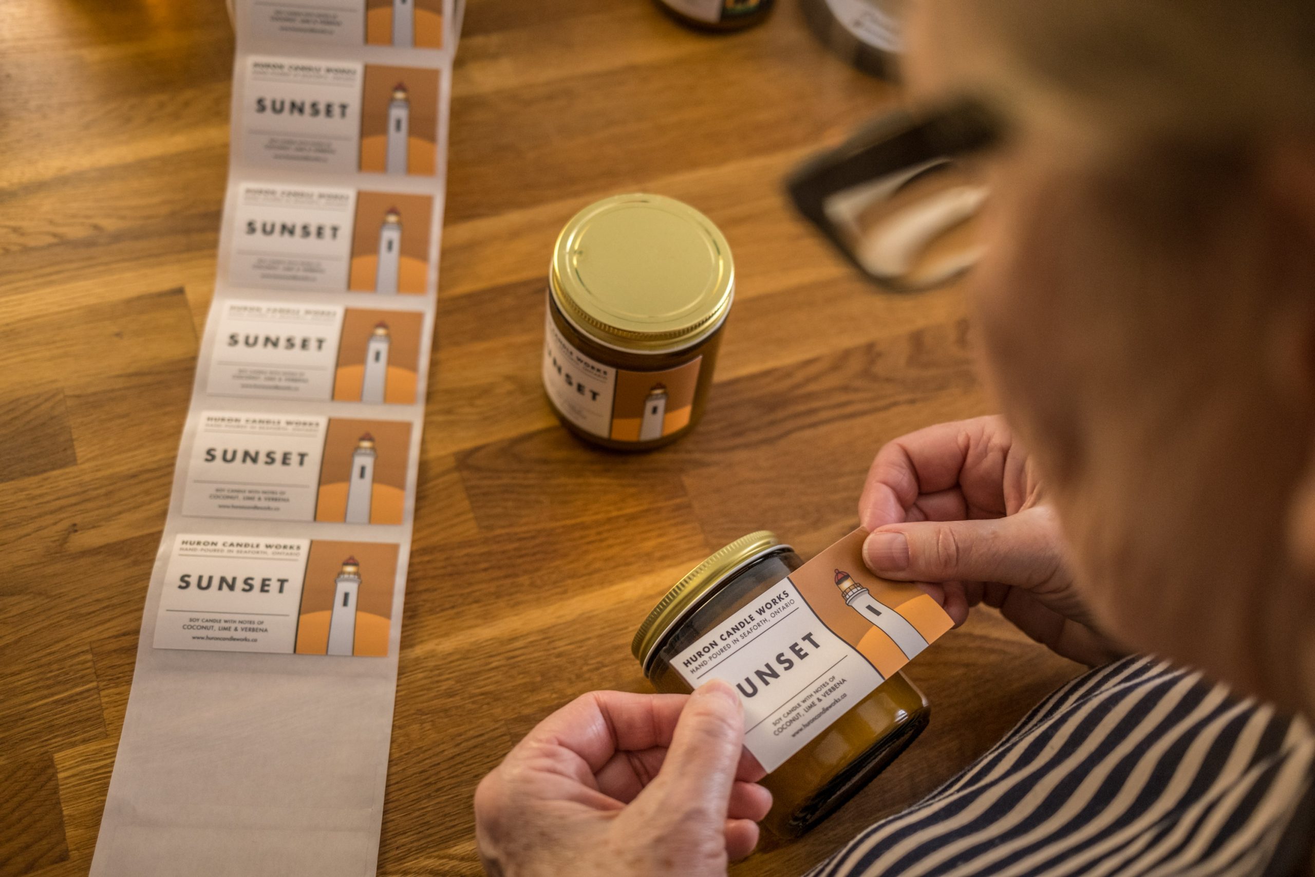 Photo of a roll of stickers and hands applying sticker label to candle jar