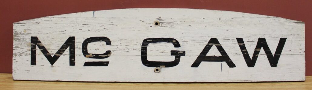 Wooden sign, painted white. Black letters M-C-G-A-W