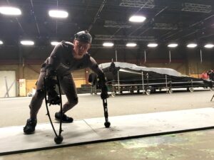 Photograph of Jesse Sturdy behind the scenes inside movie studio, wearing apparatus and dots for motion capture technology.