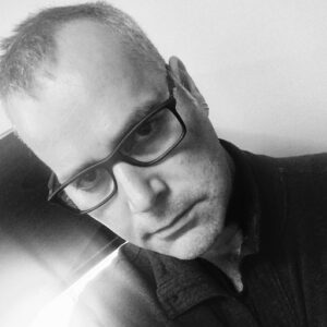 Black and white headshot photo of man wearing glasses.