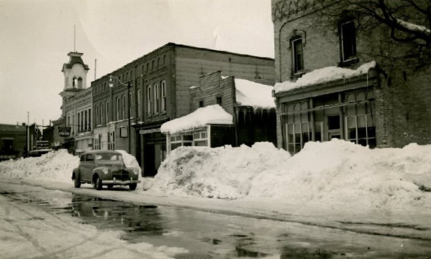 Historic black and white image showing main street Wingham with the Lyceum Theatre in the distance. The street is lined with snow banks.